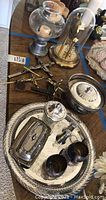 Photo showing metal crucifixes, vintage dome clock, silver-plated dinnerware pieces including tray, cups, dome covered dish, and candle holder with candle.