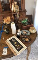 Photo of a wooden table displaying various decorative items including statues, vases, framed art, costume jewelry box, and ceramic pieces.