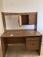 Front angled view of wooden desk with hutch, drawers and cabinet doors visible. Shows wear and condition of surfaces.