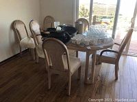 View of the entire dining set including wooden table and six upholstered chairs with light fabric, showing wear and use.