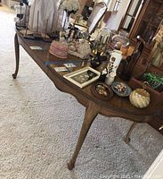 Side view of a solid wood dining table showing cabriole legs and wood grain surface with various decorative items on top.