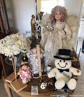 Wide view of lot items showing large angel doll, smaller dolls, plush doll, flower arrangements, wood doll stands, and decorative items.