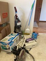 Photo of cleaning supplies and vacuums including a boxed Hurricane 360 Spin Mop, multiple vacuum cleaners, and a steam inhaler box.