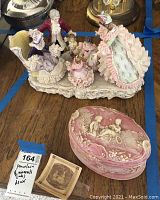 Porcelain Victorian figurine group with men, women, and children in period dress on cream-colored base, next to pink jasper decorative box with white reliefs.
