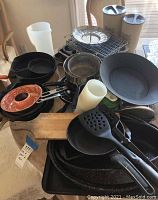 Photo shows a variety of cast iron cookware items including pans, a copper-colored bundt cake pan, plastic spatulas, a wire rack, and two tan thermos-style beverage containers.