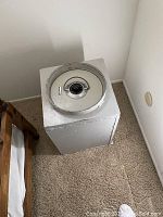 Closed view of white painted metal safe next to a wooden bed frame, showing the round metal combination dial on top.