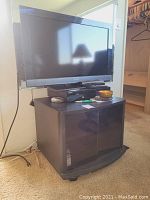 Sony Bravia TV on top of a black curved glass door TV stand with Samsung VHS player on the stand. The TV remote and a small bowl are visible on the TV stand.