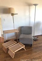 Wide view of all items in the lot: gray chair, wooden table, wooden folding TV trays, beige wall lamp, white floor lamp, power strip visible on floor.