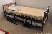 Wooden twin bed frame with mattress and four black metal detachable side railings placed in front.