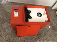 Orange vintage safe with white front panel and combination dial lock, door partially removed to show locking mechanism.