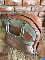 Vintage Brunswick bowling ball bag showing brown and grey body with zipper and handle, placed against a brick wall