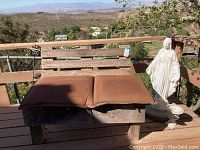 Photo showing wood bench with rust-colored cushions, white garden statue next to it, small vase and solar light truck on the side