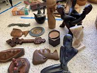 Photo showing a variety of carved wooden figures and decorative items laid on carpet, including multiple busts, plates, and carvings.