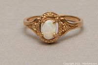 Front view showing the oval white opal set in ornate 10kt gold with textured details on the setting.