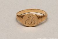 Front view of gold ring showing monogram 'J' on oval face with engraved sides.