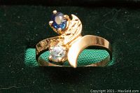 Ring shown from the front with sapphire and aquamarine stones and crescent design on gold band, on green background.