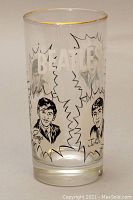 Front angle view of the clear drinking glass showing The Beatles text and illustrated portraits of band members with gold rim.