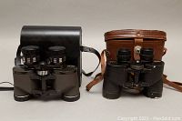 Two pairs of binoculars side by side with cases, Skyline binoculars on the left with black case, Harrison binoculars on right with brown leather case.