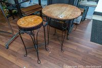 Photo showing two stools and one table with wooden tops and black twisted wrought iron bases, on a wood laminate floor inside a room.