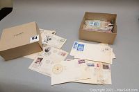 Wide view of multiple first day covers and envelopes spread out along with two boxes containing additional stamps and envelopes.