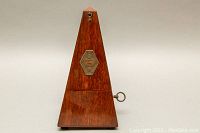Front view of the pyramid-shaped wooden metronome showing the finish and base.