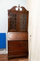 Front view of the secretary desk showing glass cabinet doors, drawers, and decorative top design