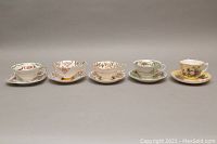 Five vintage teacup and saucer sets displayed side by side showing varied floral and gold patterns on bone china.