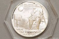Close-up of medallion side showing lunar module landing scene, American flag, two astronauts saluting, and inscription about the moon landing date and quote.