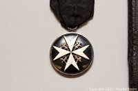 Front view of silver round medal with Maltese cross and black enamel on black ribbon.
