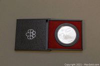 Top view of the closed black presentation box with Montreal Olympic emblem and the coin encased in plastic inside.