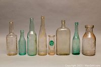 Eight vintage glass bottles lined up illustrating variety in size, shape, color, and embossing.