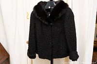 Front view of black Persian lamb fur jacket with dark mink collar, fitted on mannequin, showing button closure and curled fur texture.