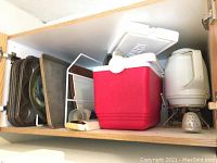 Shelf with multiple metal baking pans, cooler, and kettle