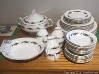 Full view of the Royal Albert High Society bone china dishes showing stacked plates, cups with handles, and serving dishes including an oval dish and lidded vegetable dish.