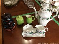 Photo shows Royal Adderley Alberta Tartan patterned coffee pot, cream and sugar on tray, lime green ceramic cream and sugar, and native-themed stacked ceramic container set.