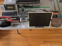 Table with various vintage electronics including computer, camera, calculator, learning system, light panel