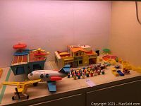 Overview of the entire lot including garage/playset, jetliner, helicopter on helipad, bush plane, and many small peg figures arranged on a flat surface.