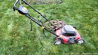 Red Homelite electric lawn mower on grass with extension cord coiled on handle, showing taped handle repair and controls.