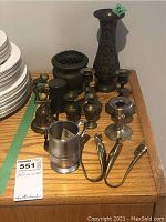 Photo showing collection of metalware items including the Crown and Rose pewter mug, brass bell, multiple brass and silver candle holders, enamel vase, metal flower frog, and rose bowl.