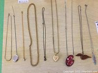 Full view of nine necklaces laid out on soft surface showing variety of chain styles and pendants.