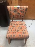 Front angled view of chair showing cubist patterned upholstery and wooden legs.