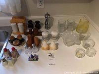 Overview of salt and pepper sets, trays, mustard jars, pepper grinder, and drinking glasses on countertop