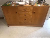 Front view of mid-century modern wood sideboard showing four central drawers with square recessed wood handles and two cabinet doors on each side.
