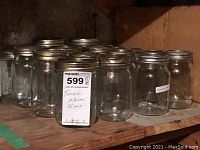 Front view of 16 small clear glass mason jars with silver metal lids arranged on a wooden shelf.