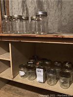 Photo of multiple small preserving jars with metal lids on two basement shelves.