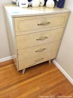 Front view of beige vintage dresser showing four drawers with metal handles and tapered legs on hardwood floor.