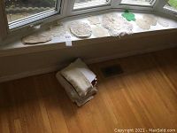 Crocheted doilies arranged on a window ledge with folded neutral colored towels on the floor below.