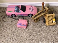 Yellow Fisher Price excavator toy with pink toy Corvette and pink wired remote control.