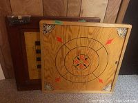 Two wooden Crokinole game boards, one with painted playing surface and corner decorations, the other with a checkerboard design on one side.