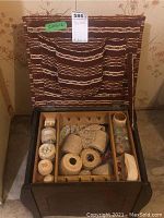 Photo of open vintage wooden sewing basket showing yarns, threads, and other materials organized in compartments, with fabric-lined lid showing pockets.